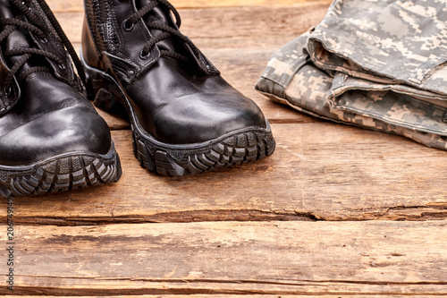 Extreme close up black soldier boots. Military camouflage clothes. Wooden desk surface background. © DenisProduction.com