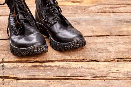 Pair of black leather soldier boots. Military shoes un wooden table.