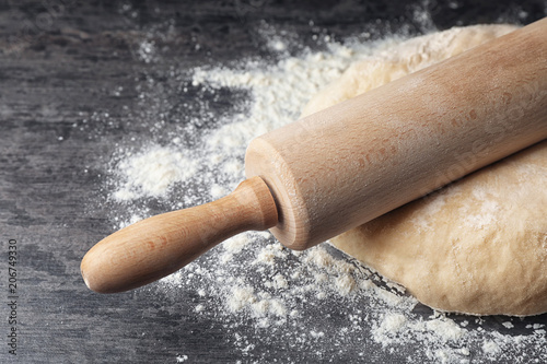 Raw wheat dough with flour and rolling pin on table, closeup photo