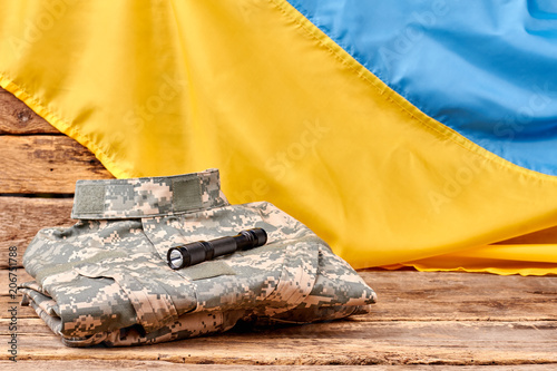 Folded camoulfage clothes and torch. Ukrainian flag on wooden background. photo