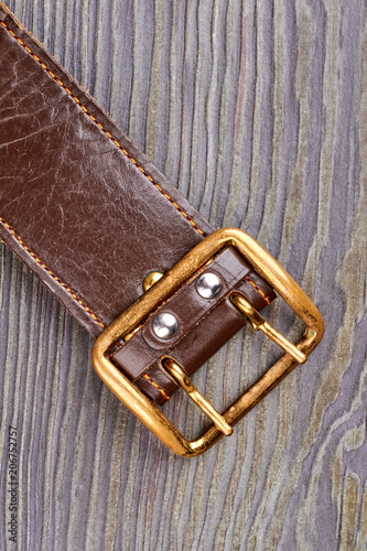 Brown leather belt close up. Golden buckle. Grey wood background.