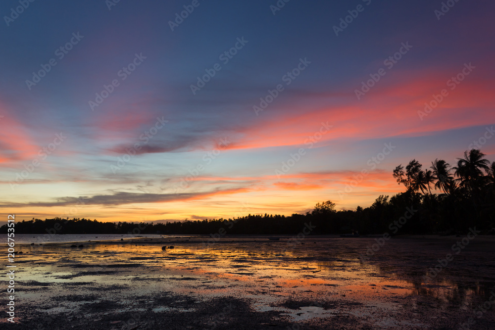Colorful, peaceful sunset landscape on the beach in the island of Koh Phangan, Thailand. Soft pink and blue colors of the sky reflect on shallow water in low tide. Summer paradise, travel vacation