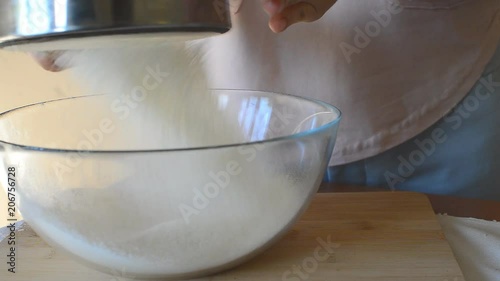 sifting the flour through a sieve to knead the dough in a transparent bowl photo