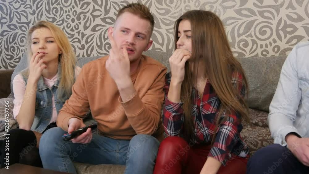 Group of young friends watching television together on couch, communicating, using cell phones Group of young friends watching television together on couch, communicating, using cell phones