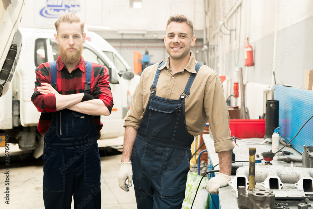 Obraz premium Portrait of young Caucasian male car mechanics in uniform standing in service garage and looking at camera