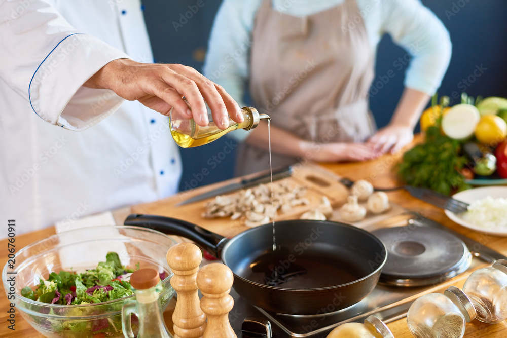 Close-up of male chef pouring oil into the pan - obrazy, fototapety, plakaty 