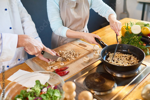 Two cooks cutting and frying mushrooms in the kitchen