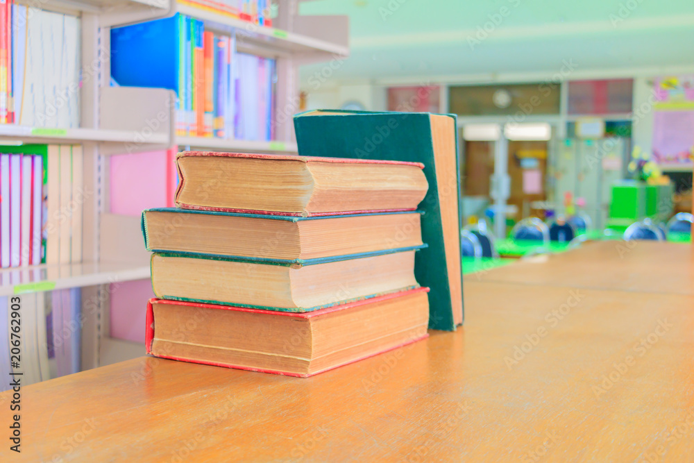 old book red - green. and heap treatise in school library on wooden table.  blurry bookshelves background. education learning concept with copy space add text