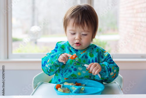Happy toddler boy eating dinner in his highchair