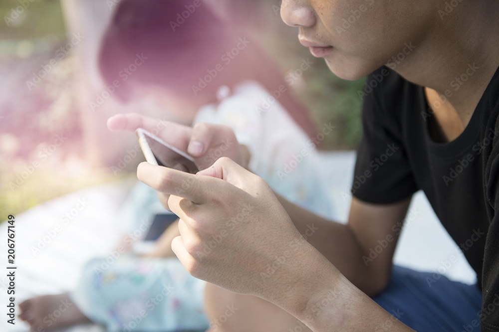 Obraz premium teen man and girl sitting near tree with mobile phone outdoors in the park.