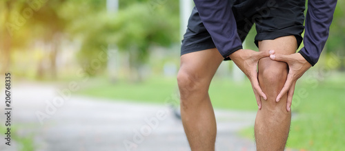 Young fitness man holding his sports leg injury, muscle painful during training. Asian runner having knee ache and problem after running and exercise outside in summer photo