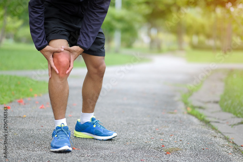 Young fitness man holding his sports leg injury, muscle painful during training. Asian runner having knee ache and problem after running and exercise outside in summer