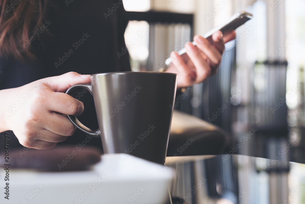 Closeup image of a woman holding and using smartphone while drinking coffee in cafe