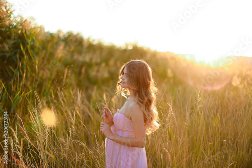 Pregnant female person standing in sun rays with steppe background, wearing pink dress. Concept of gentle summer photo session and pregnance. photo