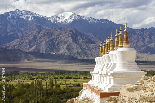 Buddhist chortens, white stupa and Himalayas mountains in the background near Shey Palace in Ladakh, India photo
