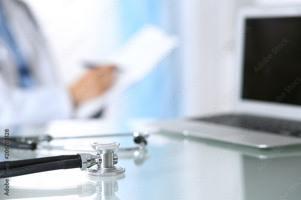 Stethoscope lying on glass desk with laptop computer at busy physician background. Medicine or pharmacy concept. Medical tools at doctor working table Stethoscope lying on glass desk with laptop computer at busy physician background. Medicine or pharmacy concept. Medical tools at doctor working table