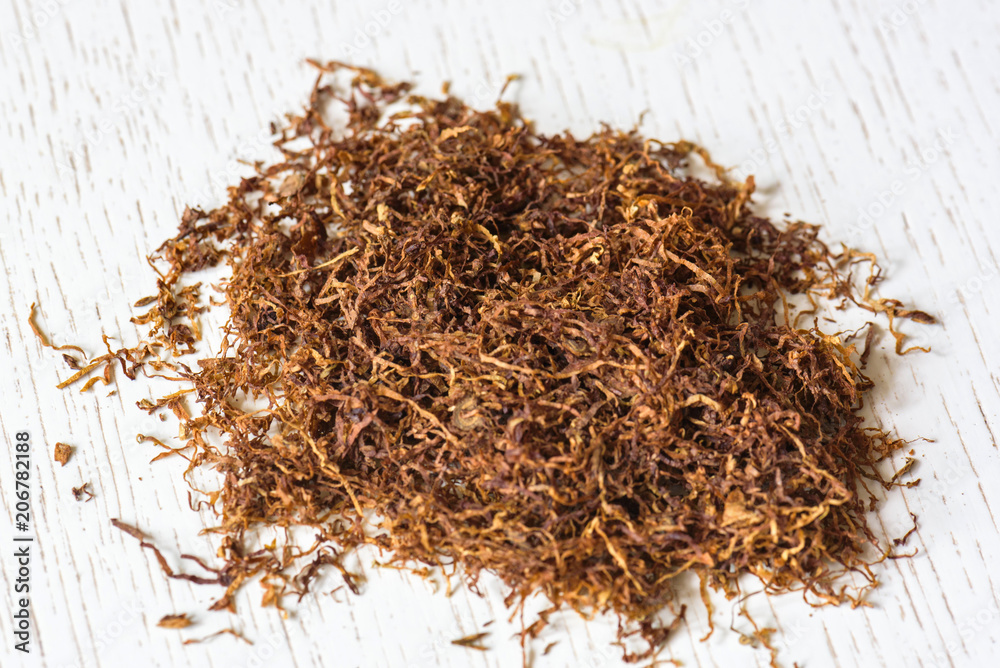 Fototapeta premium A pile of natural cigarette tobacco on a white wooden table. Nicotine addiction. Health hazard.