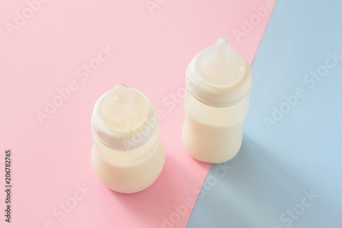 Bottle of milk for newborn baby over pink and blue pastel colors background. Maternity and baby care concept. Top view.