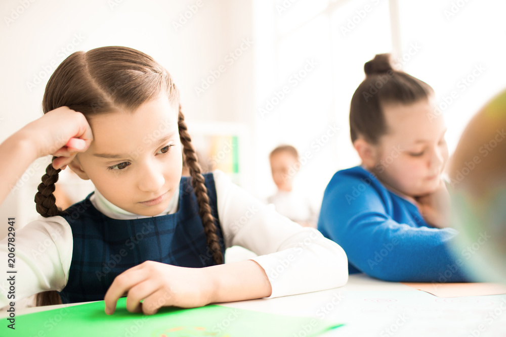 Schoolgirl puzzled by the task. She is sitting at the desk at school Schoolgirl puzzled by the task. She is sitting at the desk at school