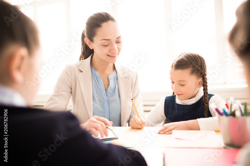 Schoolgirl studying together with teacher at the table at classroom