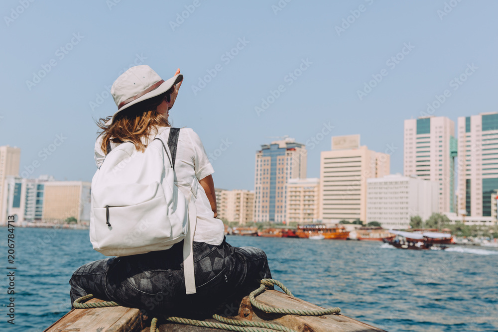 Young beautiful woman sitting at boat and looking at sea and the city DUbai