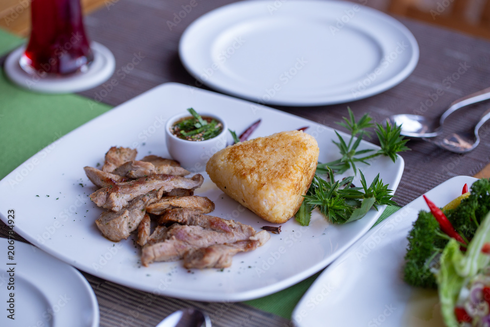 Grilled pork with grilled sticky rice and spicy sauce put on a dish decorated with vegetable on a dining table set.