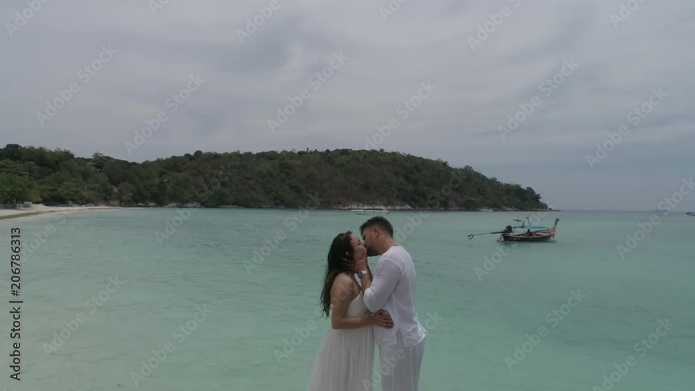 Aerial view of attractive young couple on the tropical island. Beautiful woman and man wearing white clothes embracing each other and enjoying tropical holidays vacation getaway Aerial view of attractive young couple on the tropical island. Beautiful woman and man wearing white clothes embracing each other and enjoying tropical holidays vacation getaway