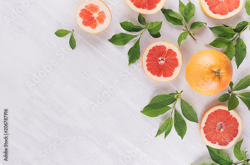 Summer colorful fresh background - slice grapefruit and green leaves on white wood board.