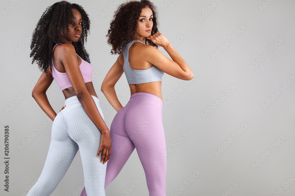 Two fitness women in sportswear isolated over gray background. Sport and fashion concept with copy space.