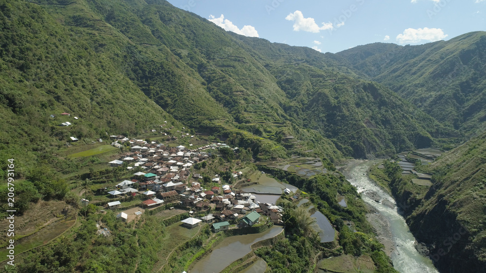 Aerial view of rice terraces and agricultural land on the slopes of the mountains. Village of farmers near rice fields in mountain valley. Mountains covered forest, trees. Cordillera region. Luzon