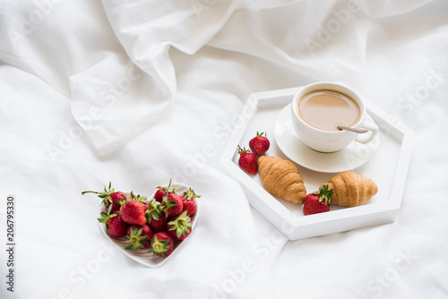 Early morning breakfast in bed, coffee and croissant with strawb