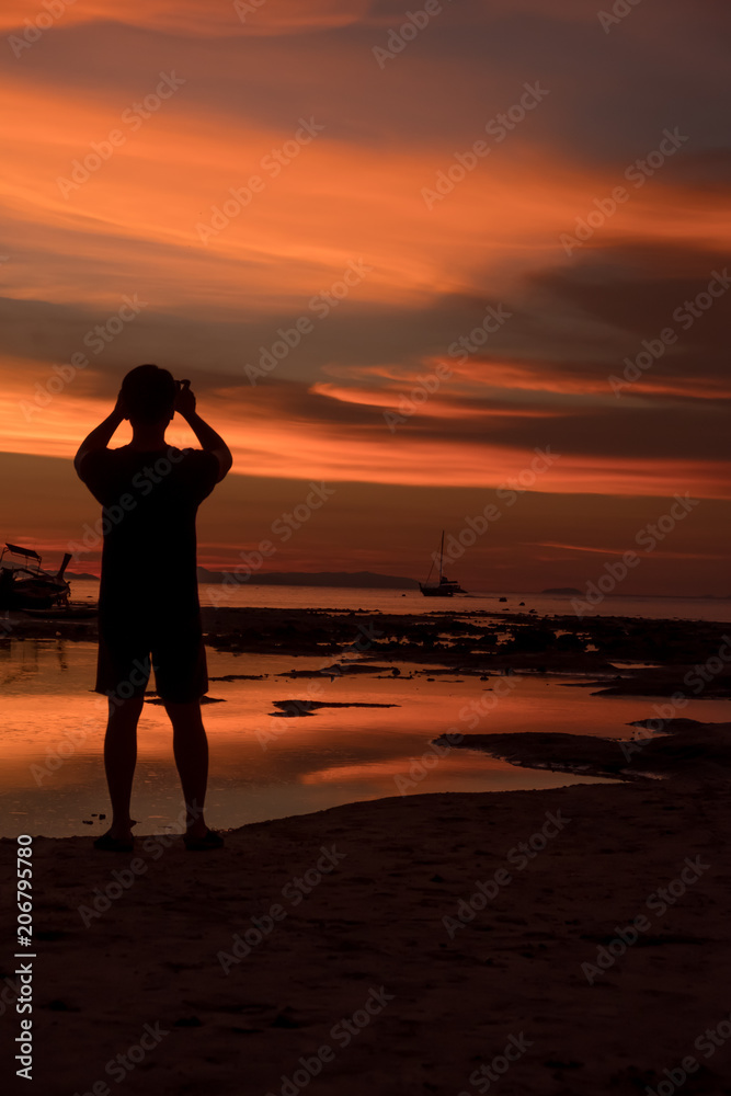 Silhouette of Man taking a sunset with a smartphone at Loh Dalum Bay, Phi Phi Island, Krabi, Thailand.