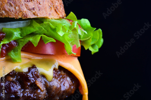 Cheese burger with grilled meat, cheese, tomato, salad and onion rings. Close-up of delicious fresh home made burger with salad and cheese on a black background