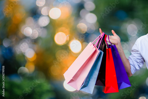 A man's hand holding shopping bags with blurred bokeh background.