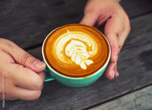 Hand women with cappuccino coffee in a green cup on wooden