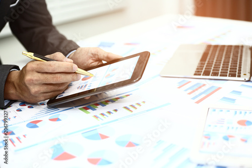 Businessman pen pointing graph chart and using a tablet for analyzing investment in his office.