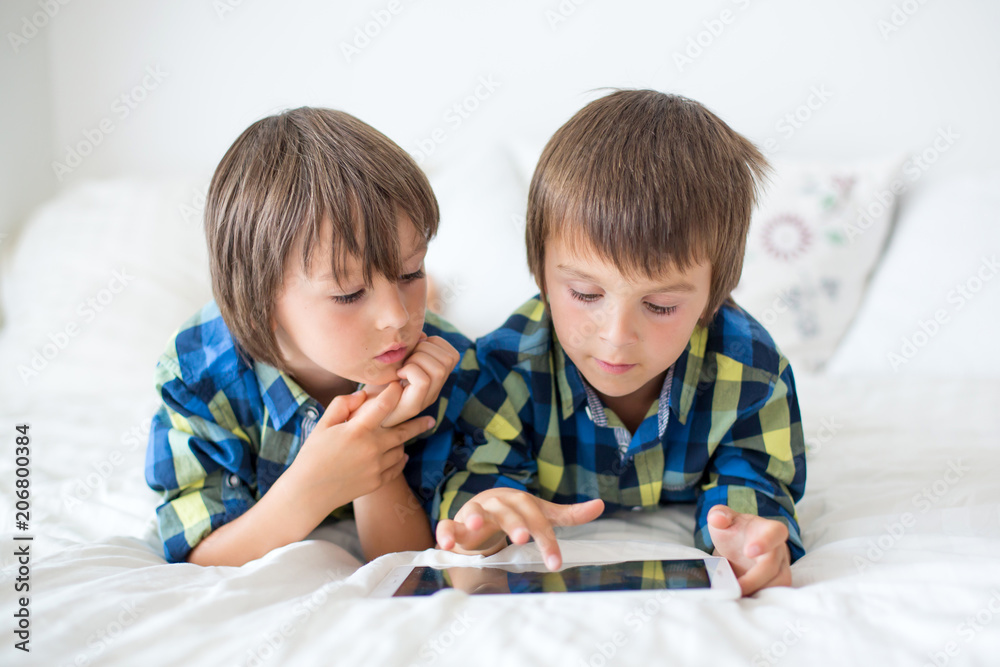 Two preschool children, boy brothers, playing at home in bed on tablet Two preschool children, boy brothers, playing at home in bed on tablet