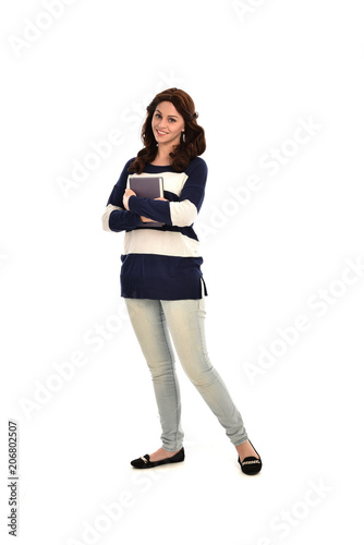 full length portrait of girl wearing striped blue and white jumper and jeans and holding a book. standing pose on white studio background © faestock