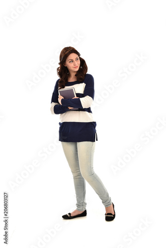 full length portrait of girl wearing striped blue and white jumper and jeans and holding a book. standing pose on white studio background © faestock