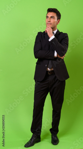 Young handsome Hispanic businessman against green background