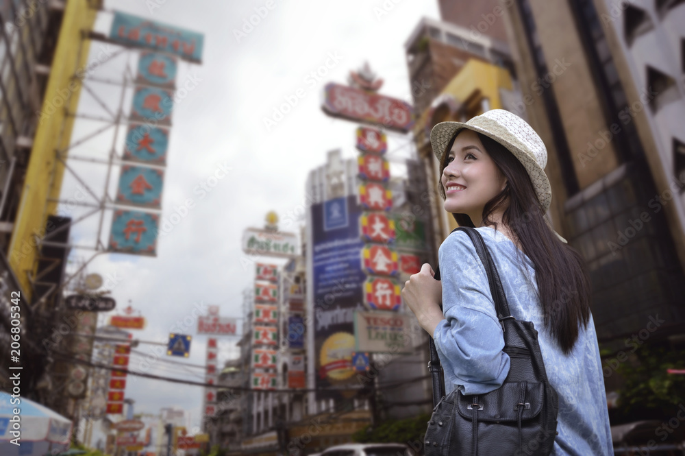 Obraz premium Young asian woman traveler with a backpack on her shoulder and travel hat walking on footpath over China town, Bangkok, Thailand, Travel holiday relaxation concept
