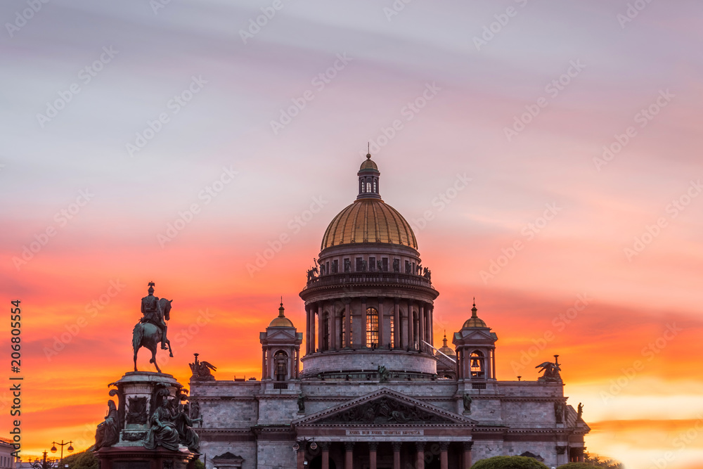 St. Isaac's Cathedral in the square, in St. Peterburg in the evening on a bright orange sunset sky, left monument-rider on horse Nikolai.