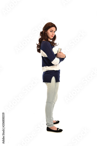 full length portrait of girl wearing striped blue and white jumper and jeans and holding a book. standing pose on white studio background