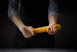 Spaghetti in the hands of a cook woman on a dark background.