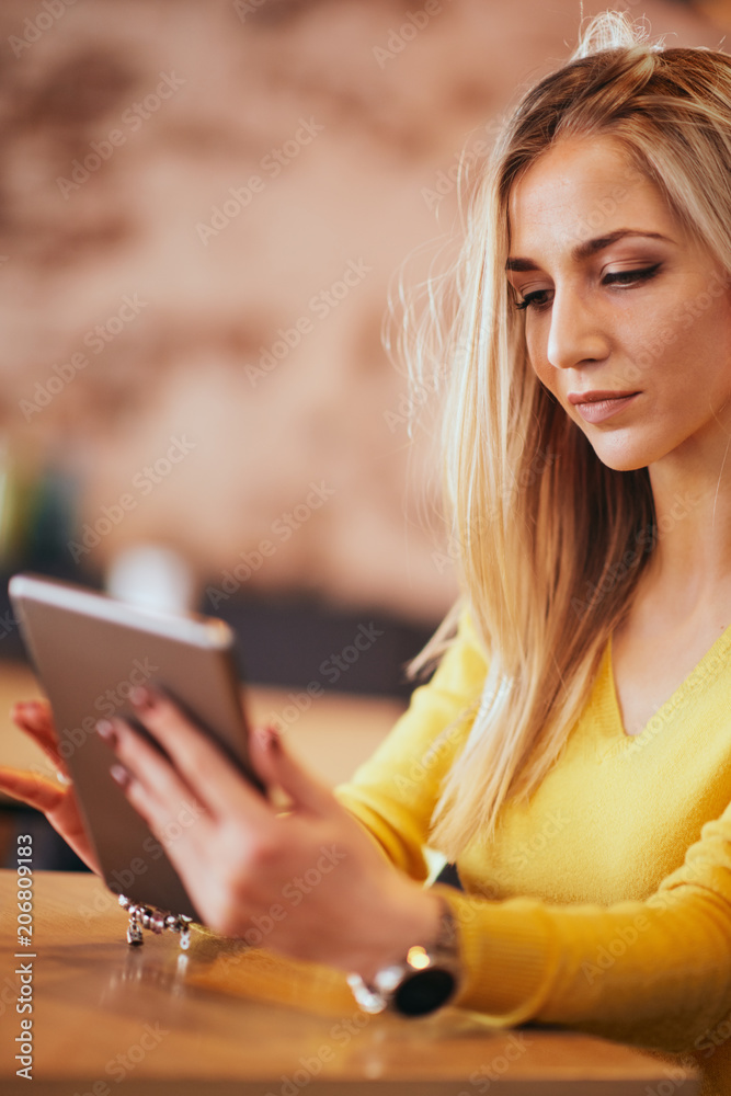 Fototapeta premium Young caucasian woman using tablet while sitting in cafe and drinking coffee.