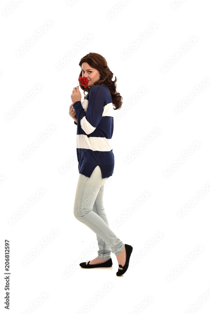 full length portrait of girl wearing striped blue and white jumper and jeans, holding a red flower. standing pose on white studio background full length portrait of girl wearing striped blue and white jumper and jeans, holding a red flower. standing pose on white studio background