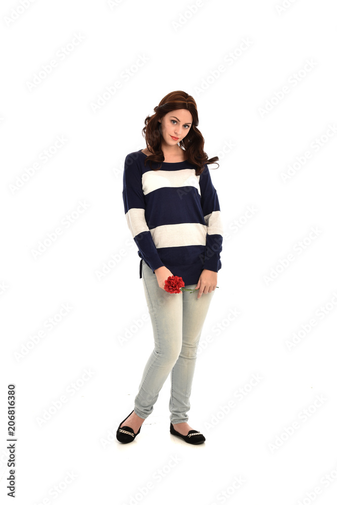 full length portrait of girl wearing striped blue and white jumper and jeans, holding a red flower. standing pose on white studio background full length portrait of girl wearing striped blue and white jumper and jeans, holding a red flower. standing pose on white studio background