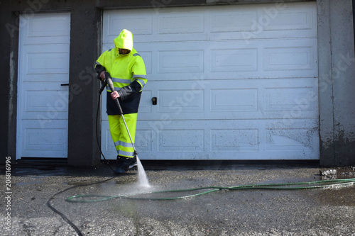 A man washes the asphalt with water. The jet of water is supplied under pressure. Flying splashes, dust and small rubbish.