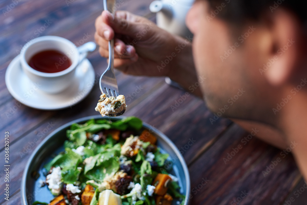 Man eating delicious salad while sitting at a bistro table - obrazy, fototapety, plakaty 
