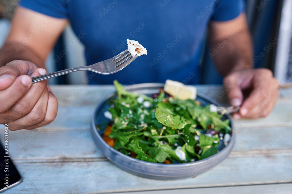 Man eating delicious salad at a rustic wooden table - obrazy, fototapety, plakaty 